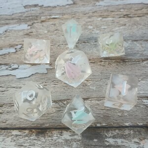 May include: Set of seven clear dice with pink, blue, and green glitter embedded inside. The dice are numbered 1 through 6 and are made of a translucent material.