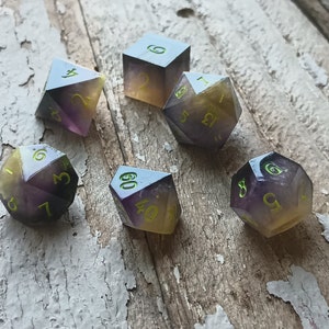 May include: Six purple and yellow dice with green numbers. The dice are on a wooden surface.
