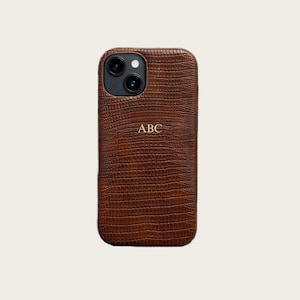 a brown leather phone case with a crocodile skin texture, featuring a personalized logo and a camera lens.