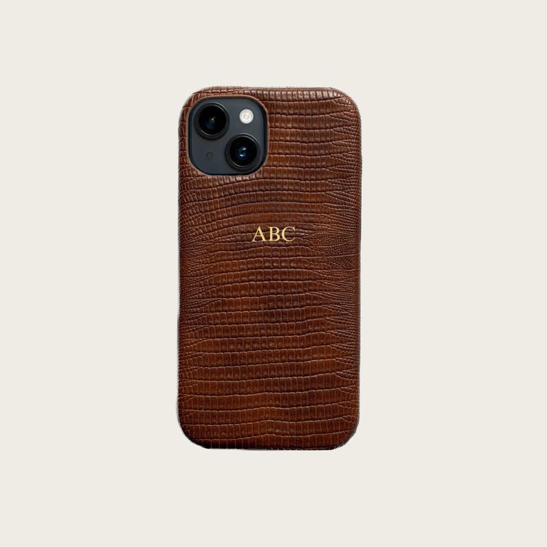 a brown leather phone case with a crocodile skin texture, featuring a personalized logo and a camera lens.