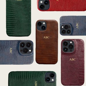 Puede incluir: Una colección de fundas para teléfono con textura en varios colores, incluyendo verde, rojo, marrón y azul. Cada funda presenta las iniciales "ABC" en letras doradas. Las fundas están diseñadas para teléfonos inteligentes y tienen un patrón de reptil.
