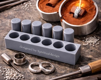 May include: A gray silicone mold with six cylindrical cavities and the text "designed by Spiritualdesign" printed on the front. The mold is accompanied by metal tools, silver granules, and two metal casting containers with brown powder.
