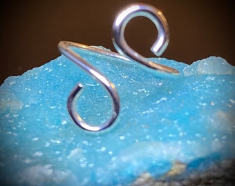 May include: A silver nose ring with a double loop design. The ring is made of wire and has a smooth, polished finish.