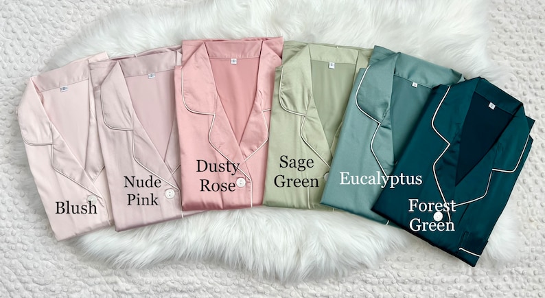 May include: Six satin pajamas in different colors: blush, nude pink, dusty rose, sage green, eucalyptus, and forest green. Each pajama top has a button closure and a collar.