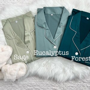 May include: Three satin pajamas in sage green, eucalyptus green, and forest green. Each pajama top has a white trim and a button closure. The text "Sage", "Eucalyptus", and "Forest" is written below each pajama top.