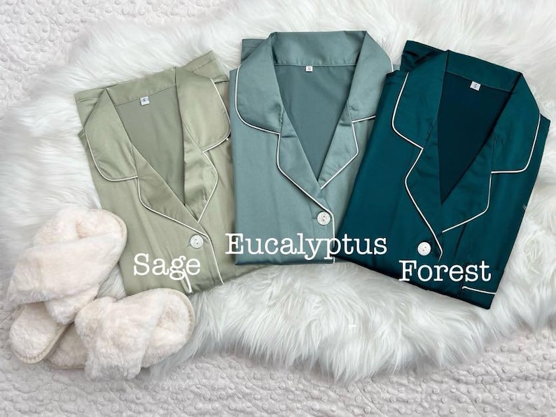 Op de afbeelding: Drie satijnen pyjama's in verschillende kleuren: saliegroen, eucalyptusgroen en bosgroen. Elk pyjama-top heeft een witte rand rond de kraag en manchetten. De tekst "Sage", "Eucalyptus" en "Forest" staat onder elk pyjama-top.