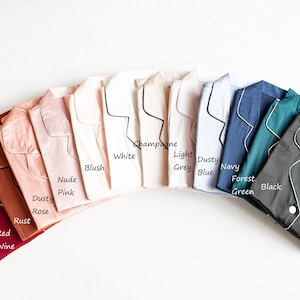 Op de afbeelding: Een verscheidenheid aan kleuren van pyjama's met een zwarte bies. De kleuren omvatten rode wijn, roest, poederroze, nude roze, blush, wit, champagne, lichtgrijs, stofvrij blauw, marine, bosgroen en zwart.