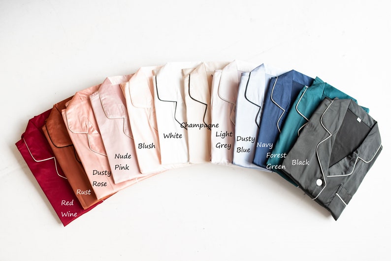 Op de afbeelding: Een verscheidenheid aan kleuren van pyjama's met een zwarte bies. De kleuren omvatten rode wijn, roest, poederroze, nude roze, blush, wit, champagne, lichtgrijs, stofvrij blauw, marine, bosgroen en zwart.