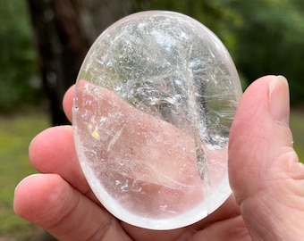 May include: A large, clear, oval-shaped crystal with a smooth, polished surface. The crystal has a slight iridescent sheen.