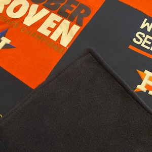 May include: A patchwork quilt with a navy blue, orange, and white color scheme. The quilt features the words "October Proven" and "World Series Champions" in a gold font.