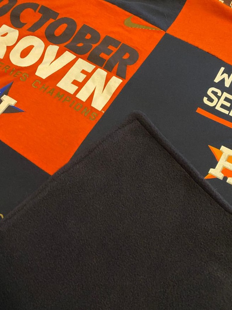 May include: A patchwork quilt with a navy blue, orange, and white color scheme. The quilt features the words "October Proven" and "World Series Champions" in a gold font.
