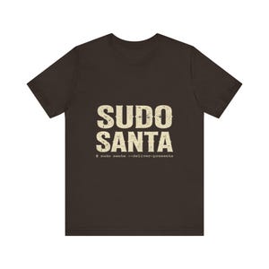 May include: A dark brown short-sleeve t-shirt featuring the text SUDO SANTA in a distressed, off-white, block-style font. Below the main text, a smaller line of text reads $ sudo santa --deliver-presents in a typewriter-style font.