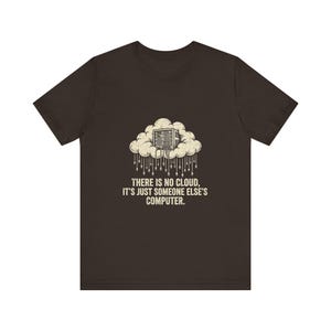 May include: A dark brown short-sleeve t-shirt featuring a graphic of a server rack inside a cloud with hanging cables. Below the graphic, the text reads: THERE IS NO CLOUD, IT'S JUST SOMEONE ELSE'S COMPUTER. The design is printed in a light cream colour.
