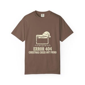 May include: A brown short-sleeved t-shirt featuring a graphic of a computer browser window wearing a Santa hat. Below the graphic, the text reads ERROR 404 CHRISTMAS CHEER NOT FOUND in a distressed, off-white font centred on the chest area.