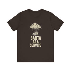 May include: A dark brown short-sleeve t-shirt featuring a graphic of a sleigh suspended from a cloud by ropes. Below the graphic, the text SANTA AS A SERVICE is printed in a distressed, off-white, sans-serif font centered on the chest.
