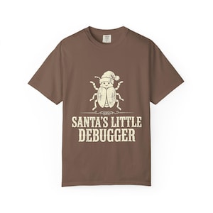 May include: A brown short-sleeved t-shirt featuring a cream-coloured graphic of a beetle wearing a Santa hat. Below the beetle, the text reads SANTA'S LITTLE DEBUGGER in a distressed, block-style font. The shirt has a crew neckline and a standard fit.