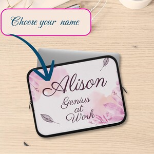 Peut inclure: Une housse d'ordinateur portable blanche avec une bordure noire, portant le nom "Alison" en écriture rose foncé, ainsi que l'expression "Genius at Work". Le design comprend des accents floraux roses à l'aquarelle et des illustrations de plumes. Le texte "Choose your name" est dans un rectangle rose.
