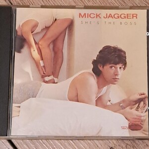 Könnte beinhalten: Ein CD-Gehäuse mit einem Foto von Mick Jagger auf dem Cover. Der Titel des Albums lautet "She's the Boss".