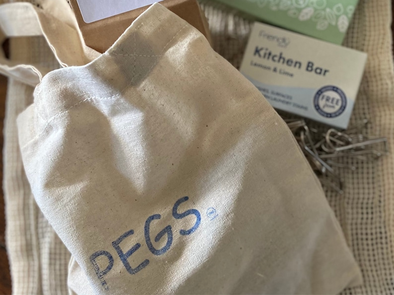 May include: A white canvas tote bag with blue lettering that says "PEGS" on the front. The bag is sitting on a brown surface.