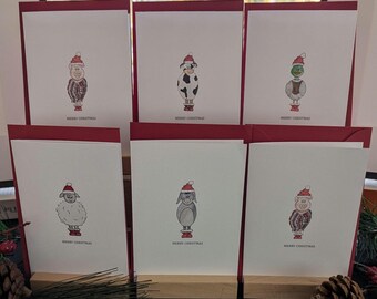 May include: A set of six white greeting cards with red envelopes, each featuring a hand-drawn illustration of a different animal wearing a Santa hat and red boots. Each card displays the text Merry Christmas at the bottom in a simple black font.