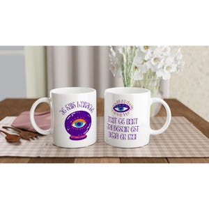 Peut inclure: Deux tasses en céramique blanche avec un motif d'œil coloré et du texte. La tasse de gauche dit "Je suis l'oracle" et présente un globe de cristal violet avec un œil à l'intérieur. La tasse de droite dit "Tout ce dont j'ai besoin est déjà en moi".