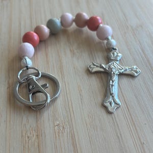 May include: A silver key chain with a small silver cross charm and a beaded loop with pink, peach, and green beads.