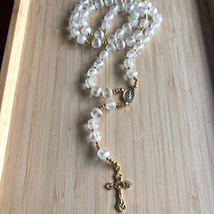 May include: A rosary with clear, faceted beads and gold-colored accents. The beads are strung together with gold-colored wire and small gold-colored beads. A gold-colored crucifix and a silver-colored medallion are at the bottom.