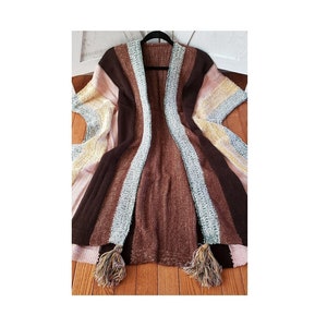 May include: A brown, pink, and yellow striped knitted cardigan with tassels. The cardigan is open in the front and has a V-neck.