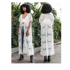 May include: A white crochet maxi dress with a tie at the waist. The dress has a scalloped hem and a lace pattern.