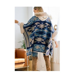 May include: A blue and brown patterned poncho with a faux fur hood and trim. The poncho has a geometric design and is made of a soft, cozy fabric.