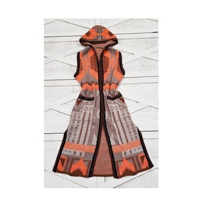 May include: A long, sleeveless cardigan with a hood. The cardigan is made of a soft, knitted fabric and features a geometric pattern in shades of orange, brown, and gray.