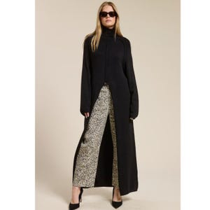 May include: A black long-sleeve knit tunic featuring a high turtleneck and a deep center front slit, paired with straight-leg trousers in a beige and black leopard print pattern. The ensemble is completed with black pointed-toe heels.