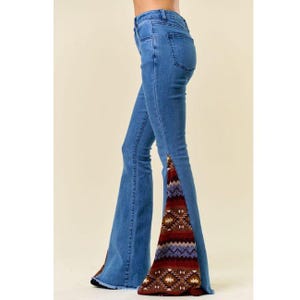 Könnte beinhalten: Hellblaue Jeans mit ausgestelltem Bein-Design. Die Jeans haben einen dekorativen Stoffeinsatz mit Muster in Rot-, Braun- und Lilatönen entlang der äußeren Nähte der ausgestellten Beine. Die Jeans haben ein klassisches Fünf-Taschen-Design.