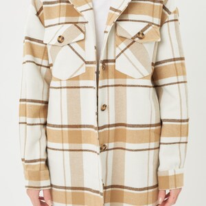 Puede incluir: Chaqueta de camisa a cuadros color crema con rayas marrones y beige. La chaqueta de manga larga tiene dos bolsillos delanteros con cierre de bot&oacute;n y una parte delantera abotonada. Tambi&eacute;n se ven el cuello y los pu&ntilde;os.