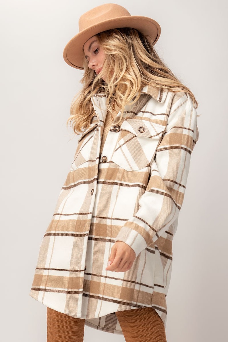 Puede incluir: Chaqueta camisa a cuadros beige con botones, dos bolsillos en el pecho y cuello. El patr&oacute;n de cuadros presenta l&iacute;neas blancas, beige y marrones. Se lleva un sombrero a juego.