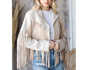 Puede incluir: Chaqueta de ante beige con largos flecos en la parte delantera y las mangas. La chaqueta tiene un cuello clásico y un corte entallado. La modelo lleva un sombrero marrón y pantalones cortos vaqueros. Una prenda de abrigo elegante.