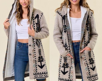 May include: A long, hooded cardigan in a neutral color with a cream-colored interior lining. The cardigan features an embroidered design in black, teal, and cream. It has a button closure and pockets.