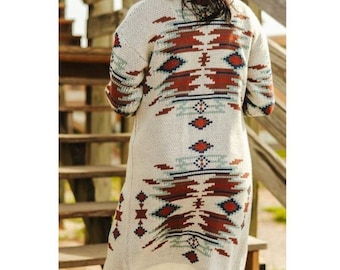 May include: Cream-colored long cardigan sweater with a Southwestern-inspired geometric pattern in shades of red, blue, and brown. The sweater features long sleeves and a knee-length design, perfect for layering. The intricate design covers the back and sleeves.