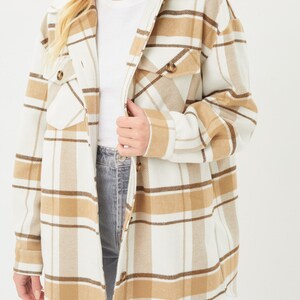 Puede incluir: Chaqueta larga a cuadros en crema, marr&oacute;n y beige. La chaqueta tiene cuello, botones y dos bolsillos delanteros. La modelo lleva una camiseta blanca y vaqueros azules.