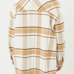 Puede incluir: Chaqueta de camisa de gran tama&ntilde;o con estampado de cuadros. La chaqueta es de color crema con l&iacute;neas de cuadros marrones y beige. Tiene cuello y pu&ntilde;os abotonados. La prenda est&aacute; hecha de una tela suave y tejida.