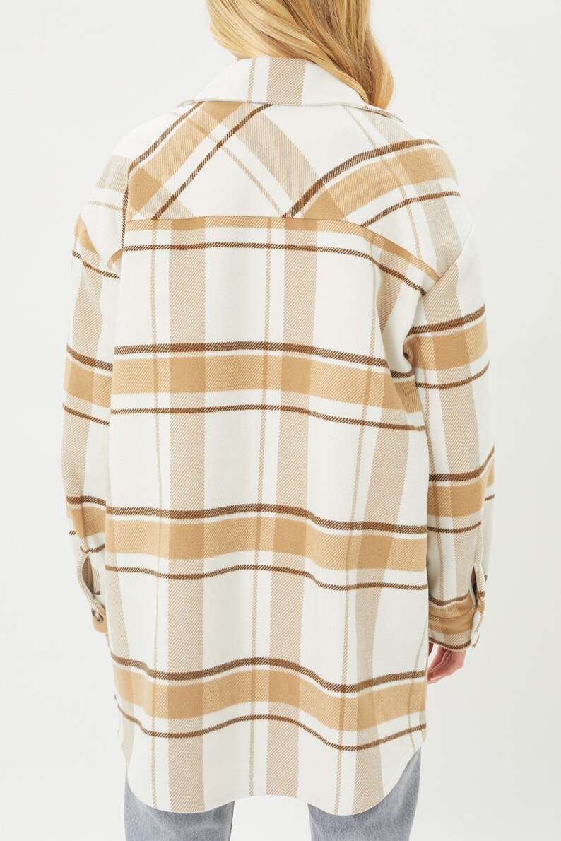 Puede incluir: Chaqueta de camisa de gran tama&ntilde;o con estampado de cuadros. La chaqueta es de color crema con l&iacute;neas de cuadros marrones y beige. Tiene cuello y pu&ntilde;os abotonados. La prenda est&aacute; hecha de una tela suave y tejida.