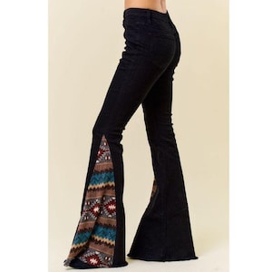 Puede incluir: Vaqueros acampanados negros con un estampado geométrico colorido en los paneles laterales. Los vaqueros tienen una cintura alta y una abertura de pierna ancha, creando un look retro y bohemio.