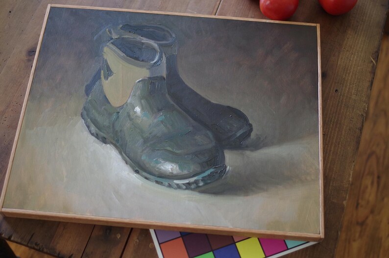 Pu&ograve; includere: Dipinto a olio di due stivali da lavoro verde scuro con finiture beige chiaro, su uno sfondo neutro. Gli stivali sono raffigurati in uno stile realistico, con trame e ombre visibili. L'opera d'arte &egrave; incorniciata in una cornice di legno marrone chiaro.