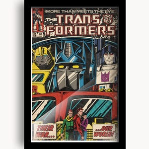 May include: Framed vintage comic book cover featuring Transformers characters. The cover art includes the text "MORE THAN MEETS THE EYE" and "THE TRANSFORMERS". The comic art has a retro style with bold colors and dynamic character designs.