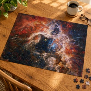 May include: A rectangular jigsaw puzzle featuring a vibrant space nebula with swirling clouds of red, orange, and blue gas, scattered stars, and a bright central star. Several loose puzzle pieces are scattered near the bottom right corner.