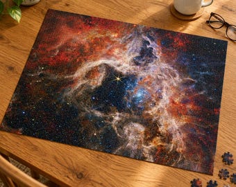 May include: A rectangular jigsaw puzzle featuring a vibrant space nebula with swirling clouds of red, orange, and blue gas, scattered stars, and a bright central star. Several loose puzzle pieces are scattered near the bottom right corner.