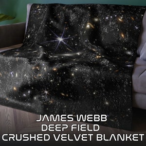 May include: A black crushed velvet blanket featuring a detailed image of the James Webb Deep Field. The blanket displays a vibrant depiction of stars and galaxies, creating a celestial theme. The text "JAMES WEBB DEEP FIELD CRUSHED VELVET BLANKET" is printed at the bottom.