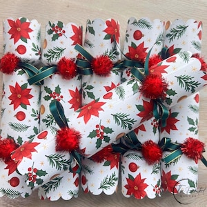 May include: A set of six cylindrical Christmas crackers featuring a white background with a repeating pattern of red poinsettias, green pine branches, and red ornaments. Each cracker is tied with a dark green ribbon and a red pom-pom.