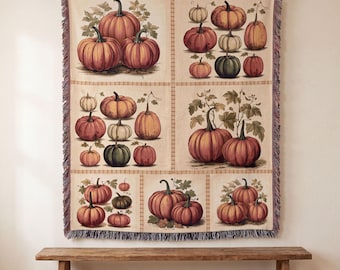 May include: A woven throw blanket featuring a grid pattern of various pumpkins in shades of orange, green, and cream. The rectangular textile has a fringed edge and displays multiple botanical illustrations of pumpkins with stems and leaves.