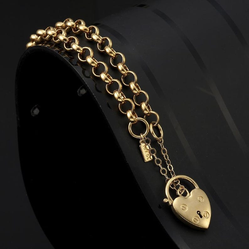 May include: A gold chain bracelet with a heart-shaped padlock charm. The chain is made of small, round links. The padlock has a keyhole and a small, decorative detail on the top.